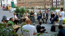 Eine Gruppe von Menschen sitzt im &ouml;ffentlichen Raum zusammen und diskutiert.