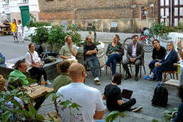 Eine Gruppe von Menschen sitzt im öffentlichen Raum zusammen und diskutiert.