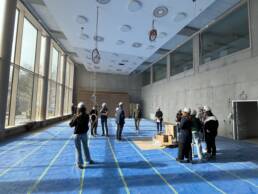 bafep 21 Saal noch im Bau mit Bodenschutzfolie und Kabeln von der Decke, dabei eine Gruppe Menschen mit Bauhelmen